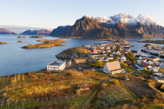 Henningsvær i Lofoten med fargerike hus og snødekte fjell ved havet, under en klar himmel.
